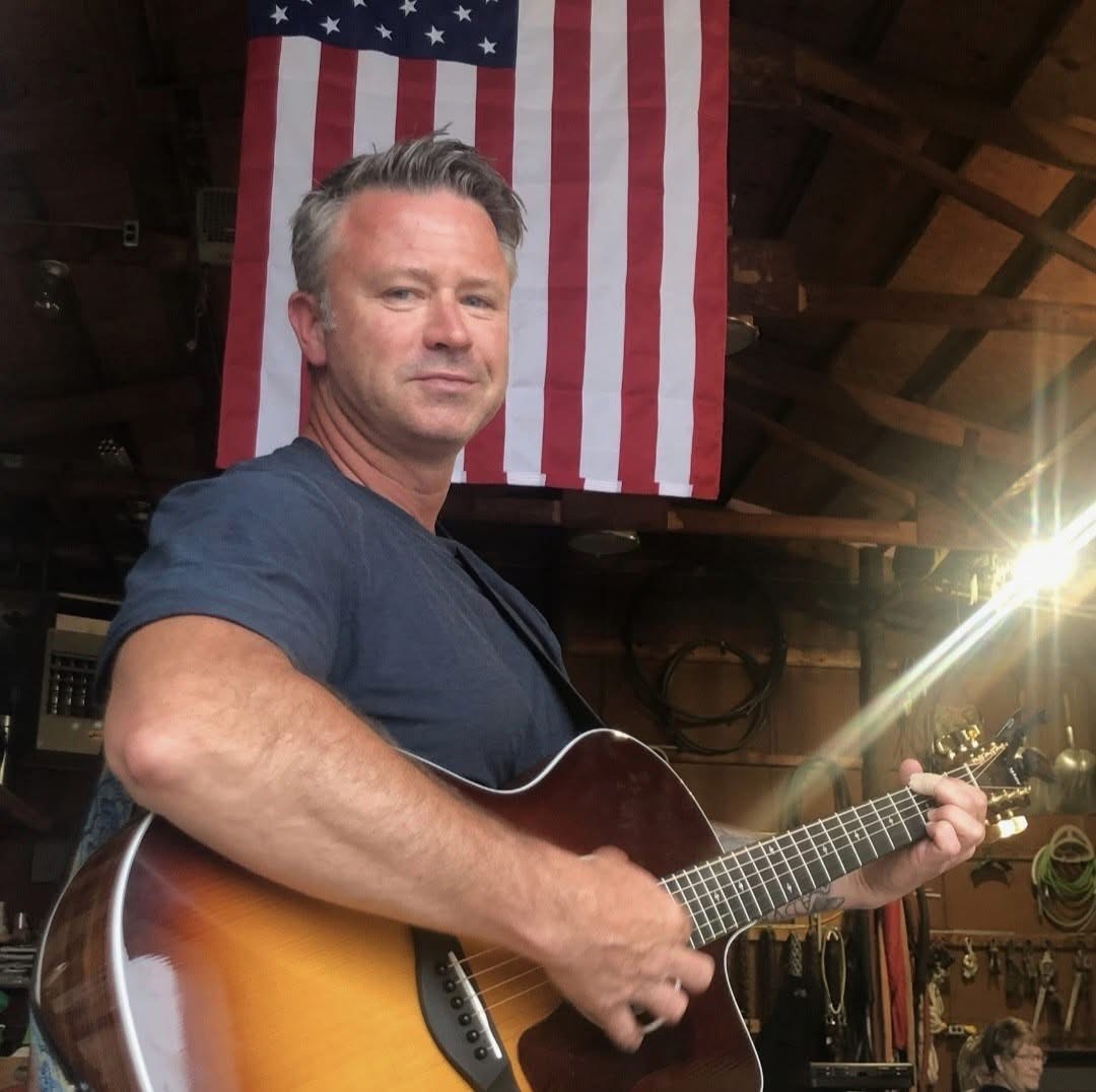 Steve Honeycutt playing guitar in front of an American flag